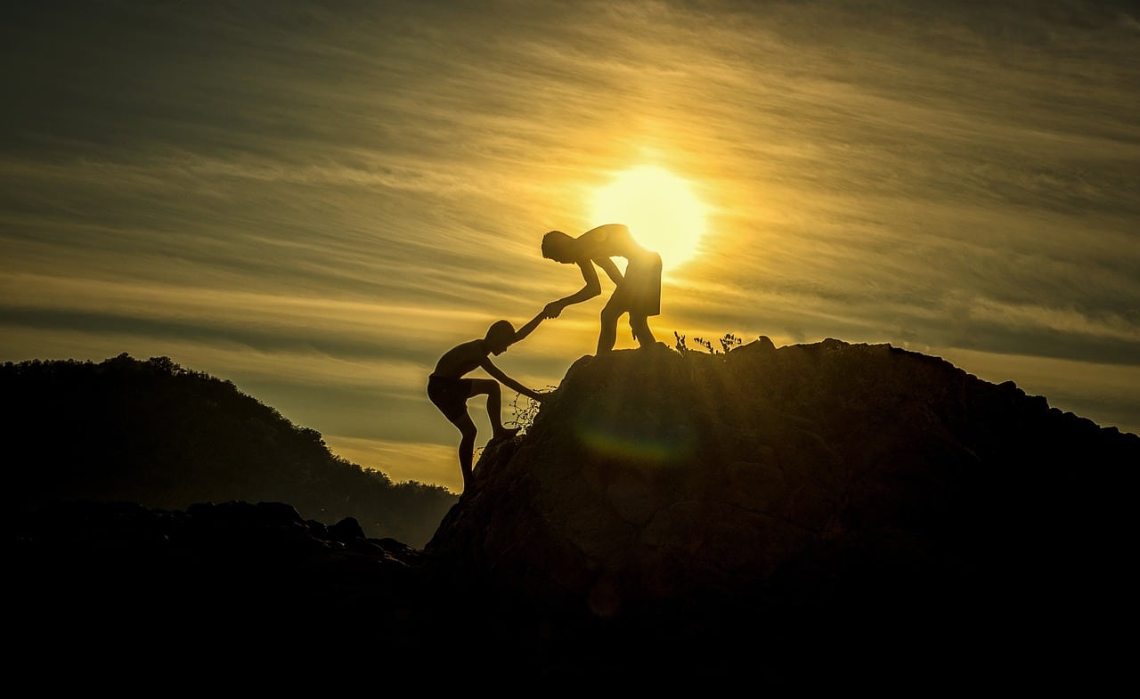 Persona ayudando a otra a escalar una montaña