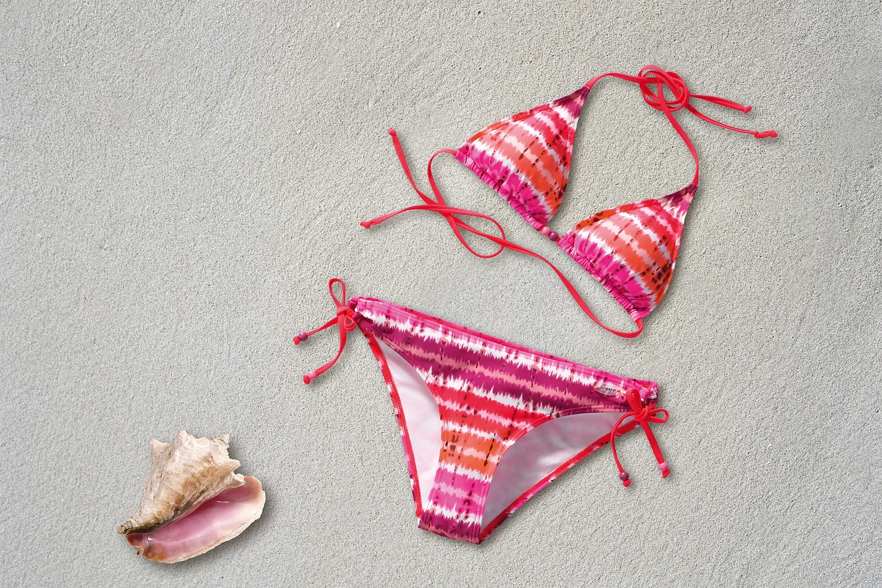 Bikini rosa y blanca a rayas sobre la arena, junto a concha marina