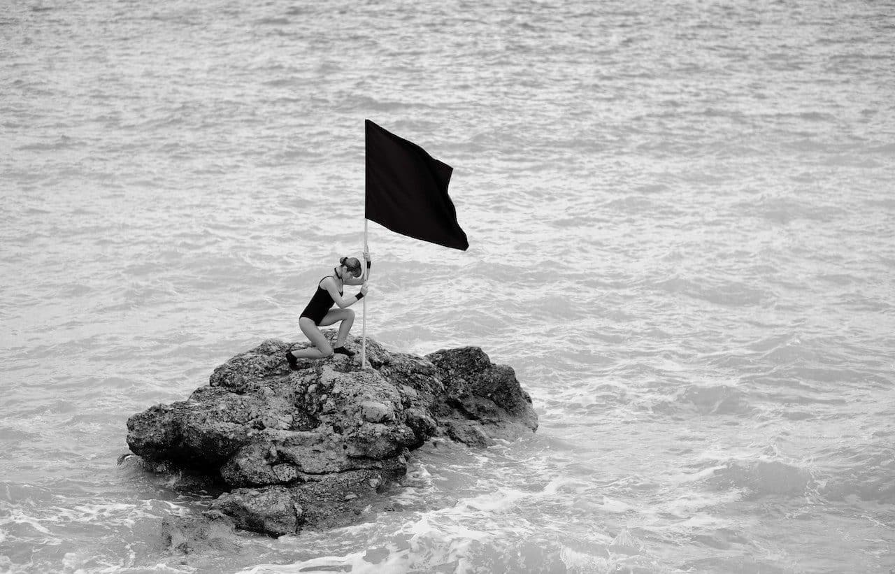 Mujer plantando una bandera sobre una roca en el mar