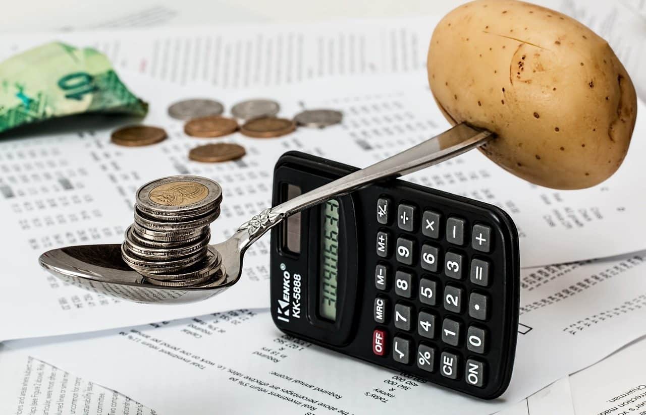 Una papa y una pila de monedas balanceándose en una cuchara, sobre una calculadora.