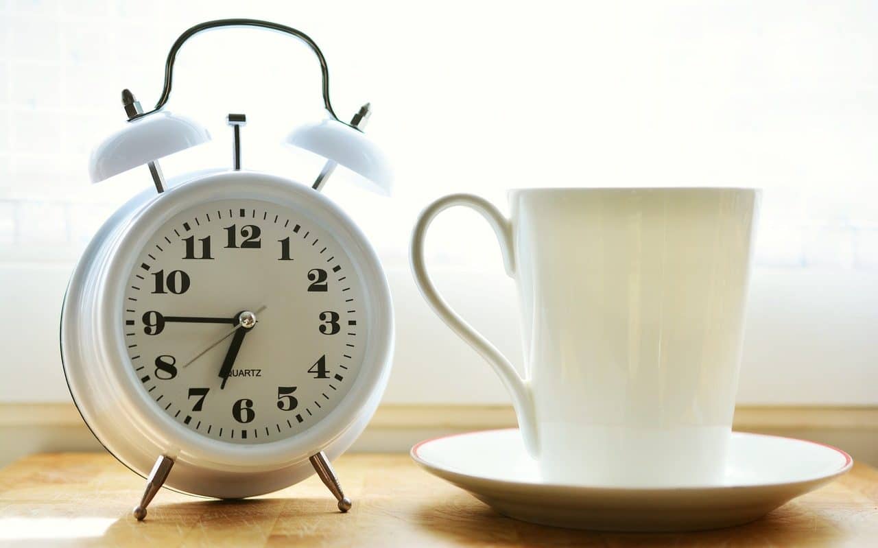 Reloj despertador junto a taza blanca