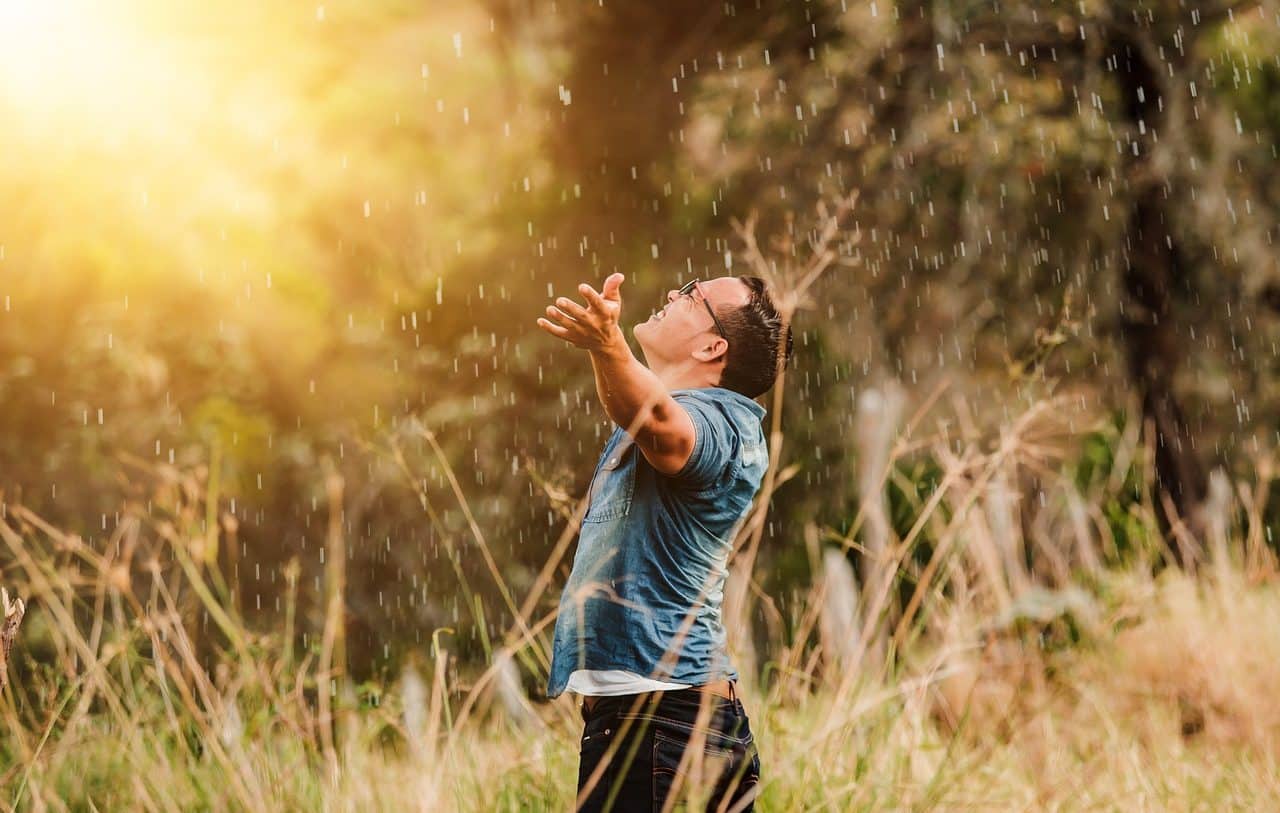 Hombre joven recibiendo la luz del Sol con los brazos abiertos