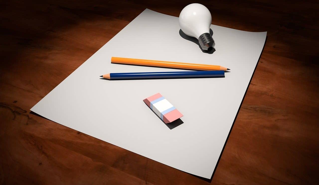 Una bombilla, dos lápices y una goma de borrar sobre una hoja de papel en blanco