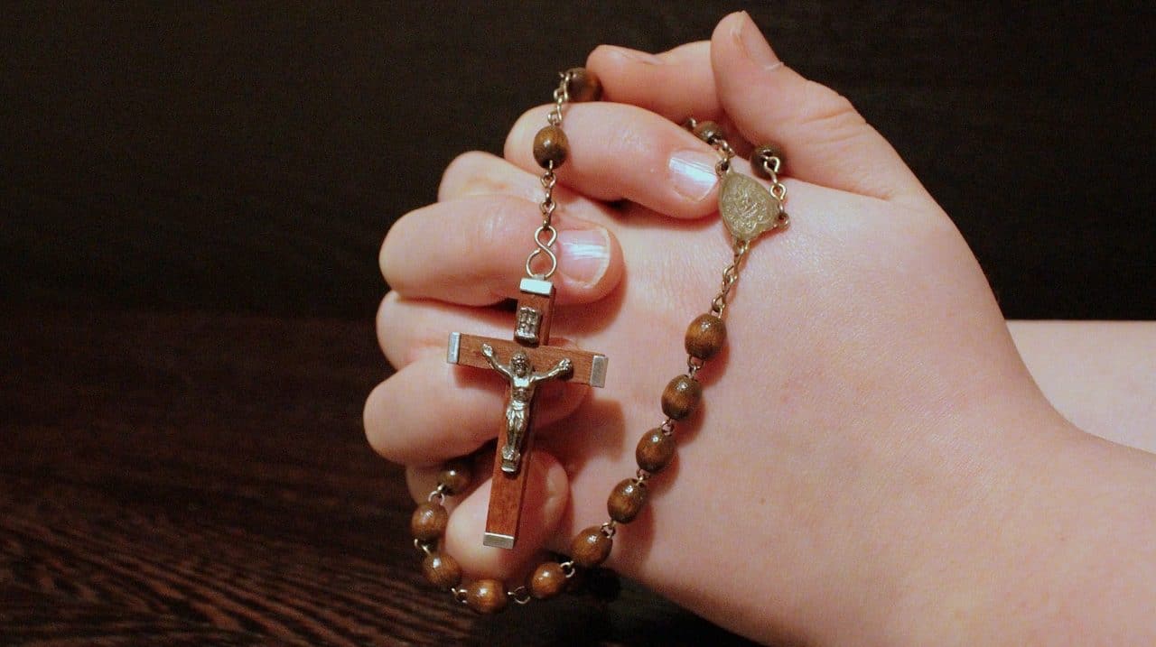 Mujer sosteniendo un rosario con sus manos unidas en posición de rezo