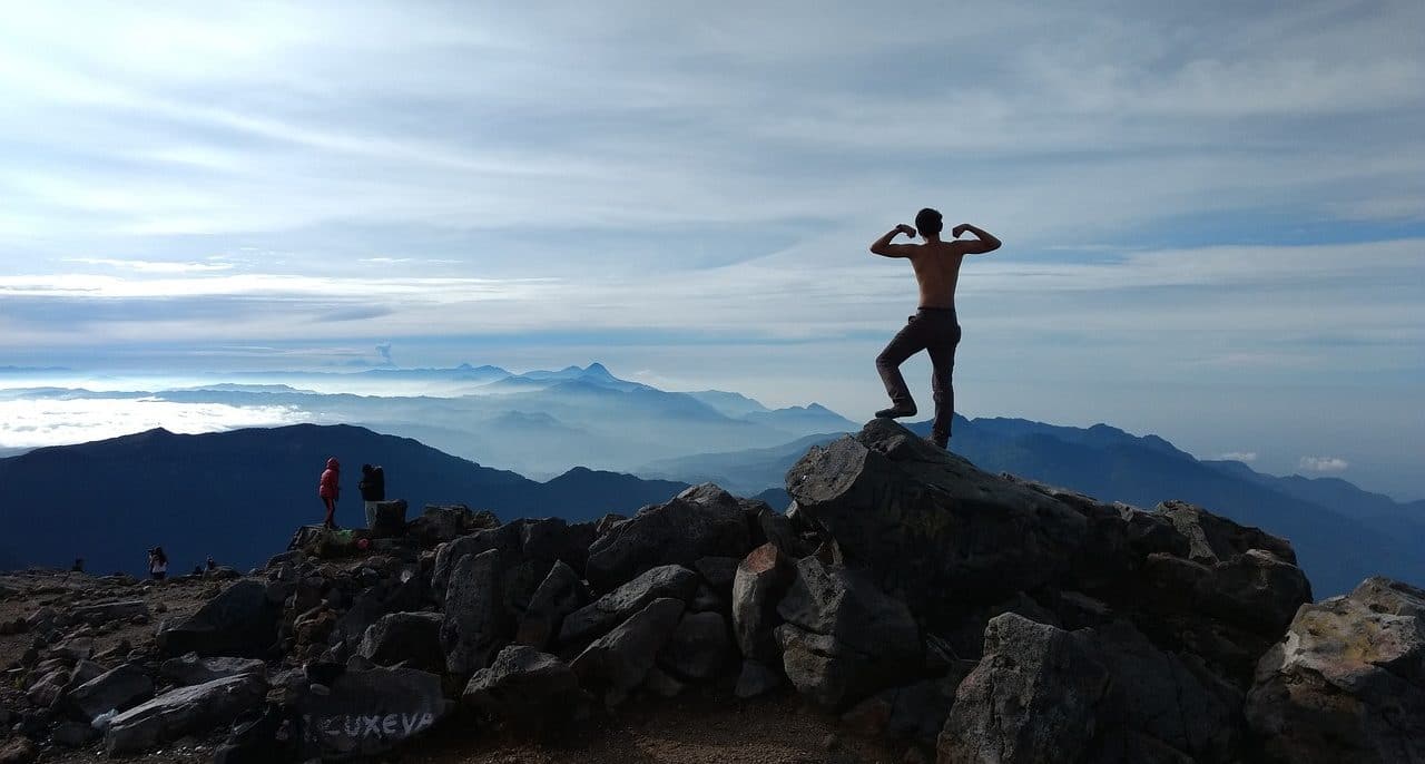 Hombre marcando sus músculos en la cima de una montaña