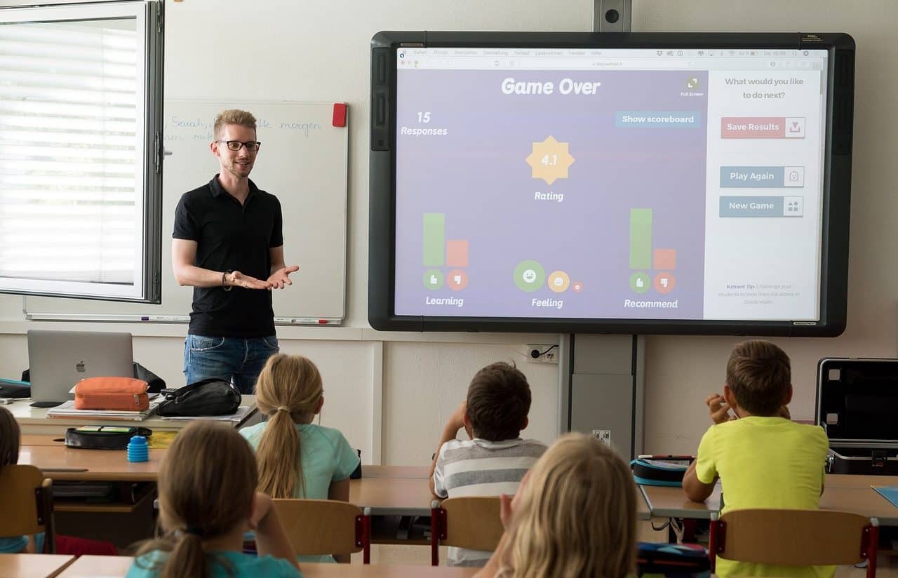 Maestro y niños en el aula mirando una presentación en un gran monitor