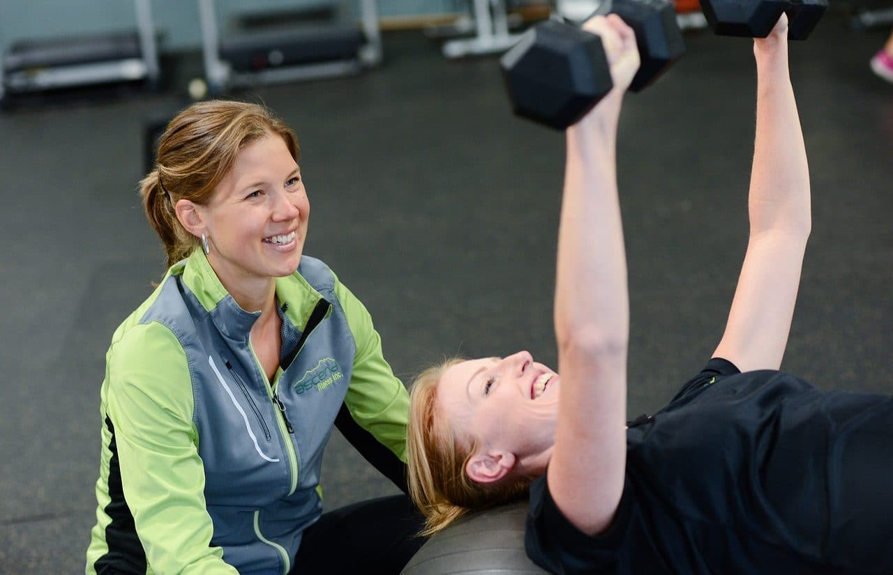 Mujer joven levantando pesas en el gimnasio con su entrenadora personal