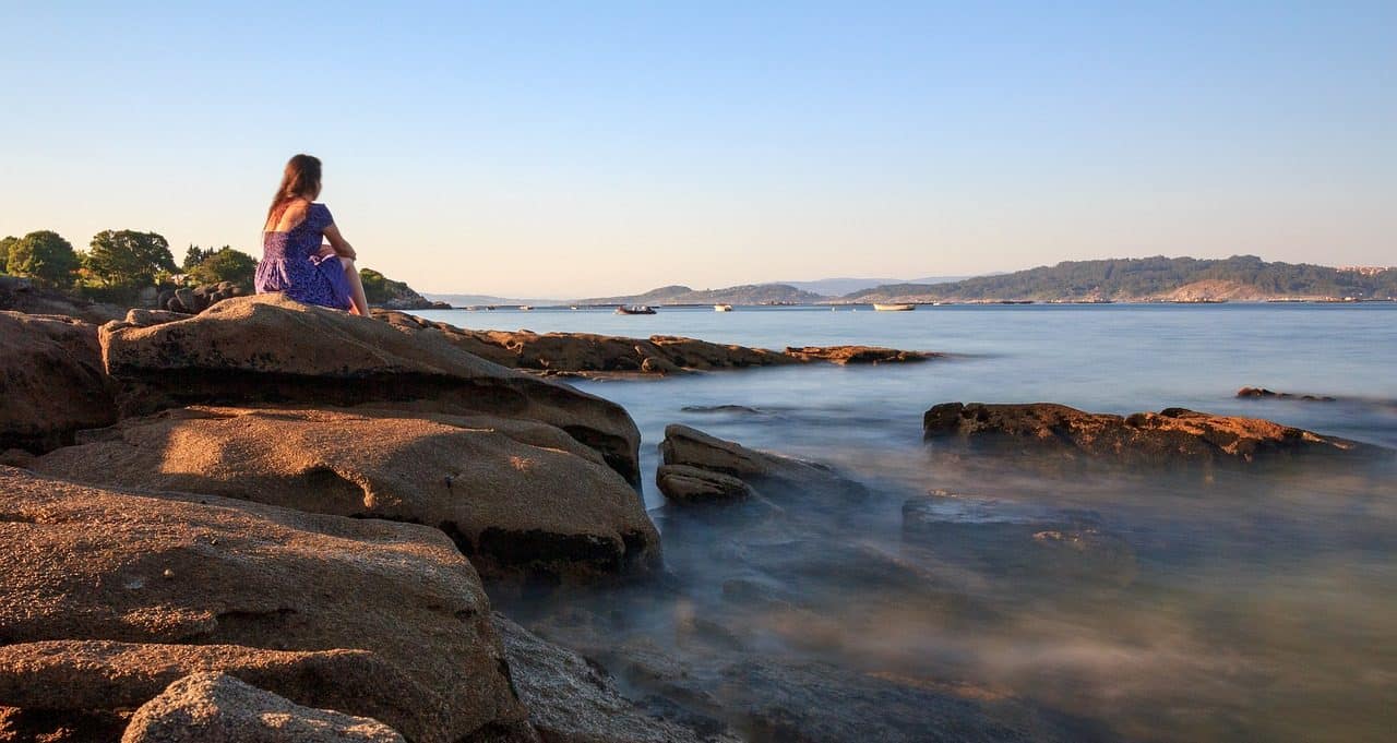 Mujer sentada sobre roca junto al agua
