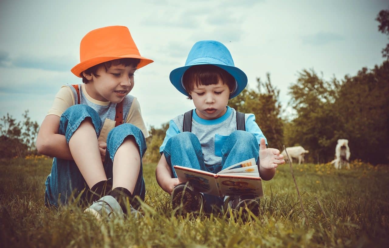 Dos niños leyendo un libro sentados en la hierba