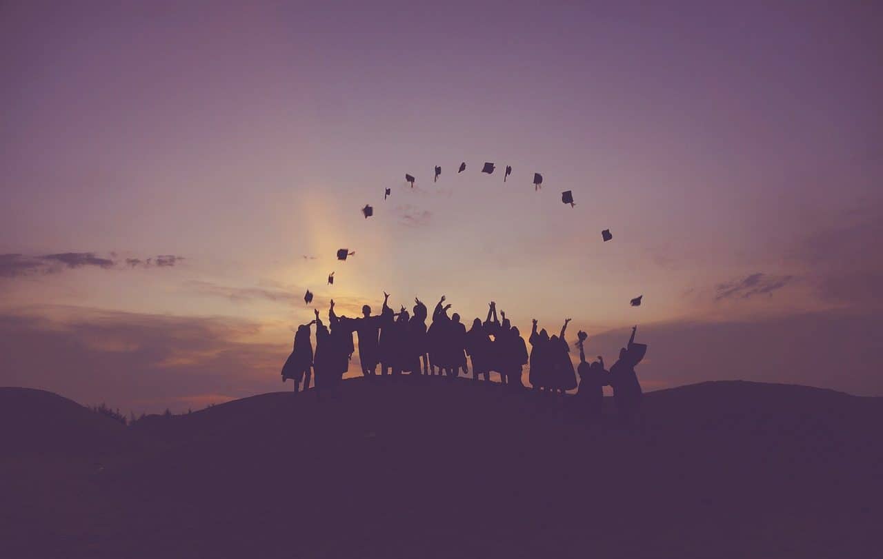 Varios estudiantes lanzando sus birretes al aire al atardecer