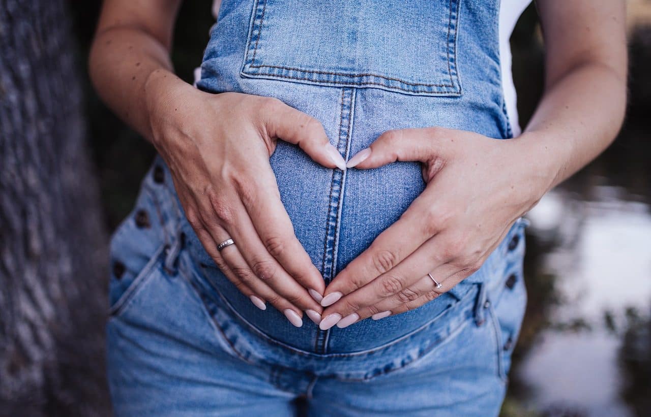 Mujer embarazada formando un corazón sobre su panza con sus manos