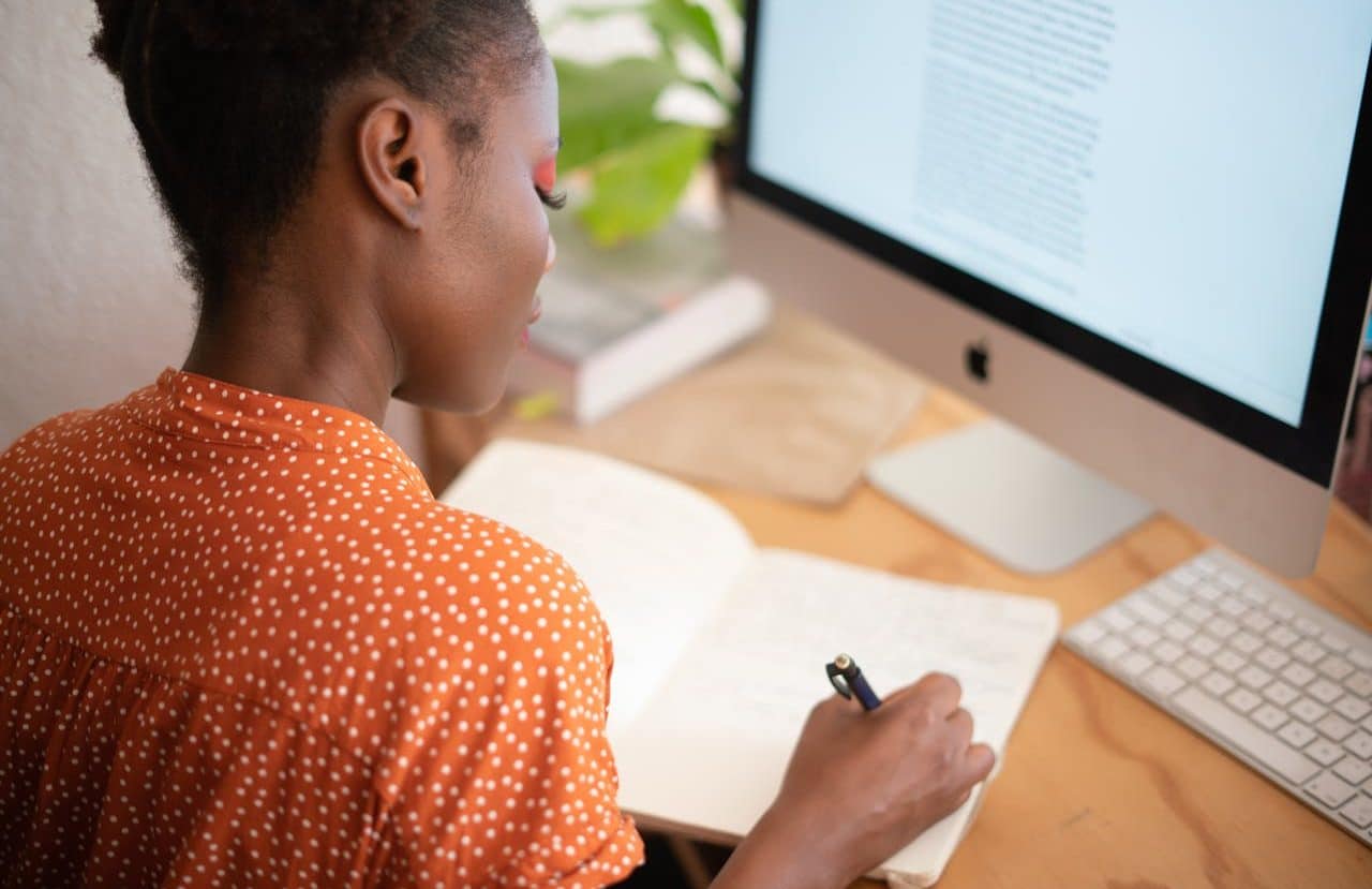 Mujer escribiendo en su cuaderno frente a su iMac.