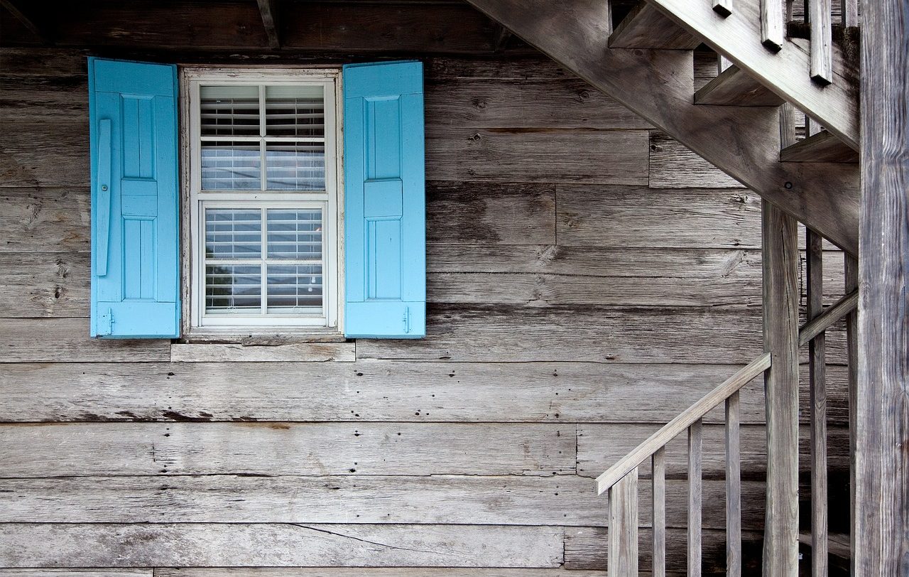 Casa de madera gris. Los postigos de la ventana son celestes.