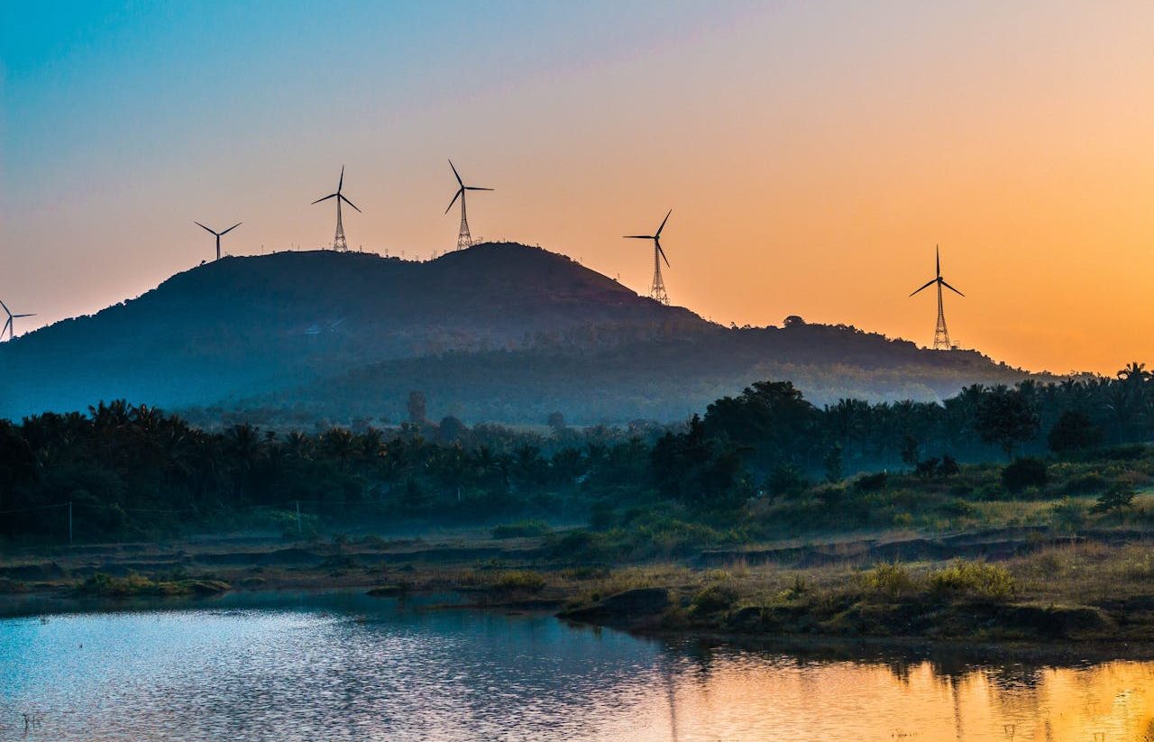 Paisaje de atardecer con turbinas eólicas sobre unas colinas.