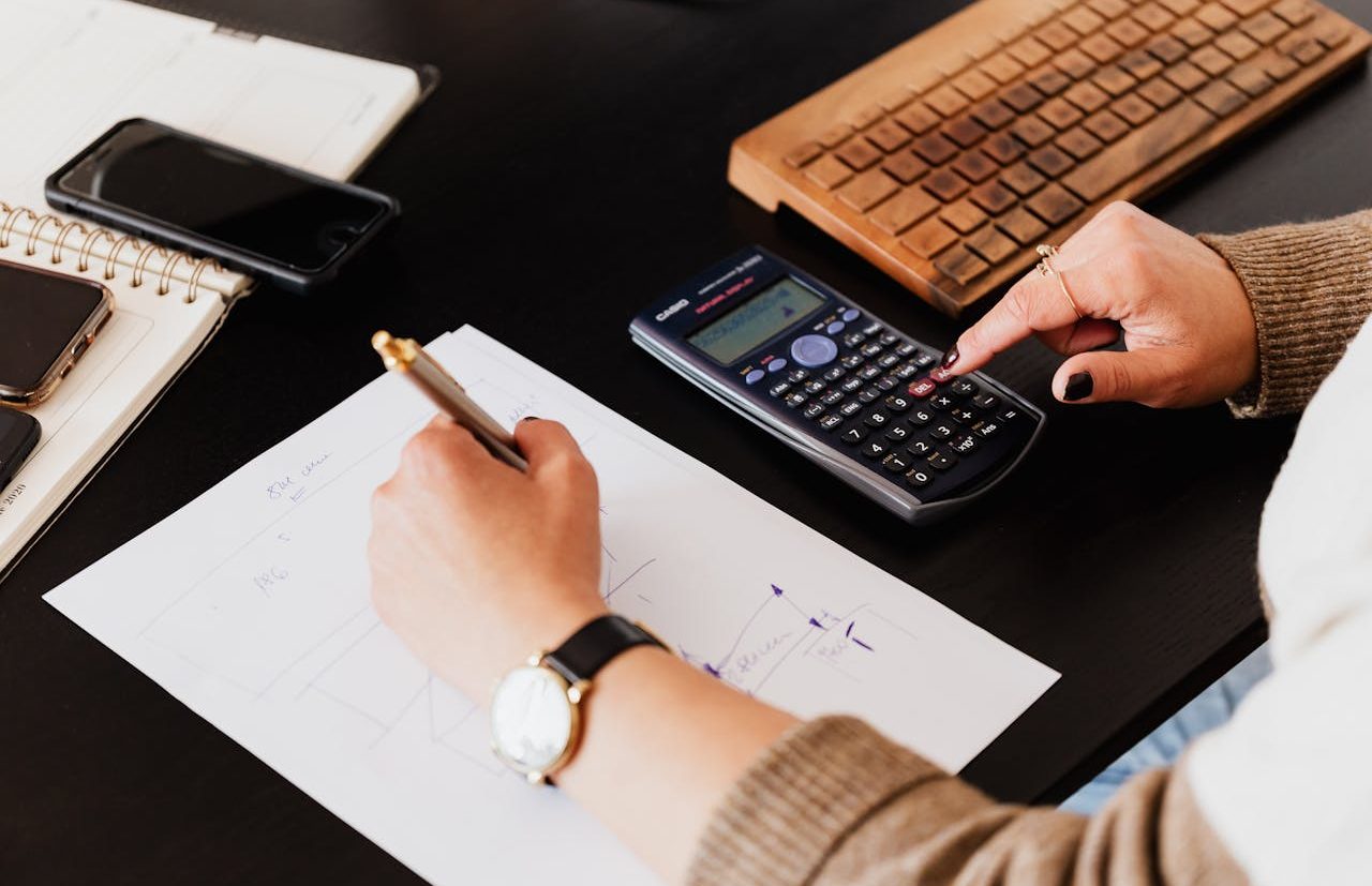 Persona usando calculadora científica y escribiendo a mano en una hoja