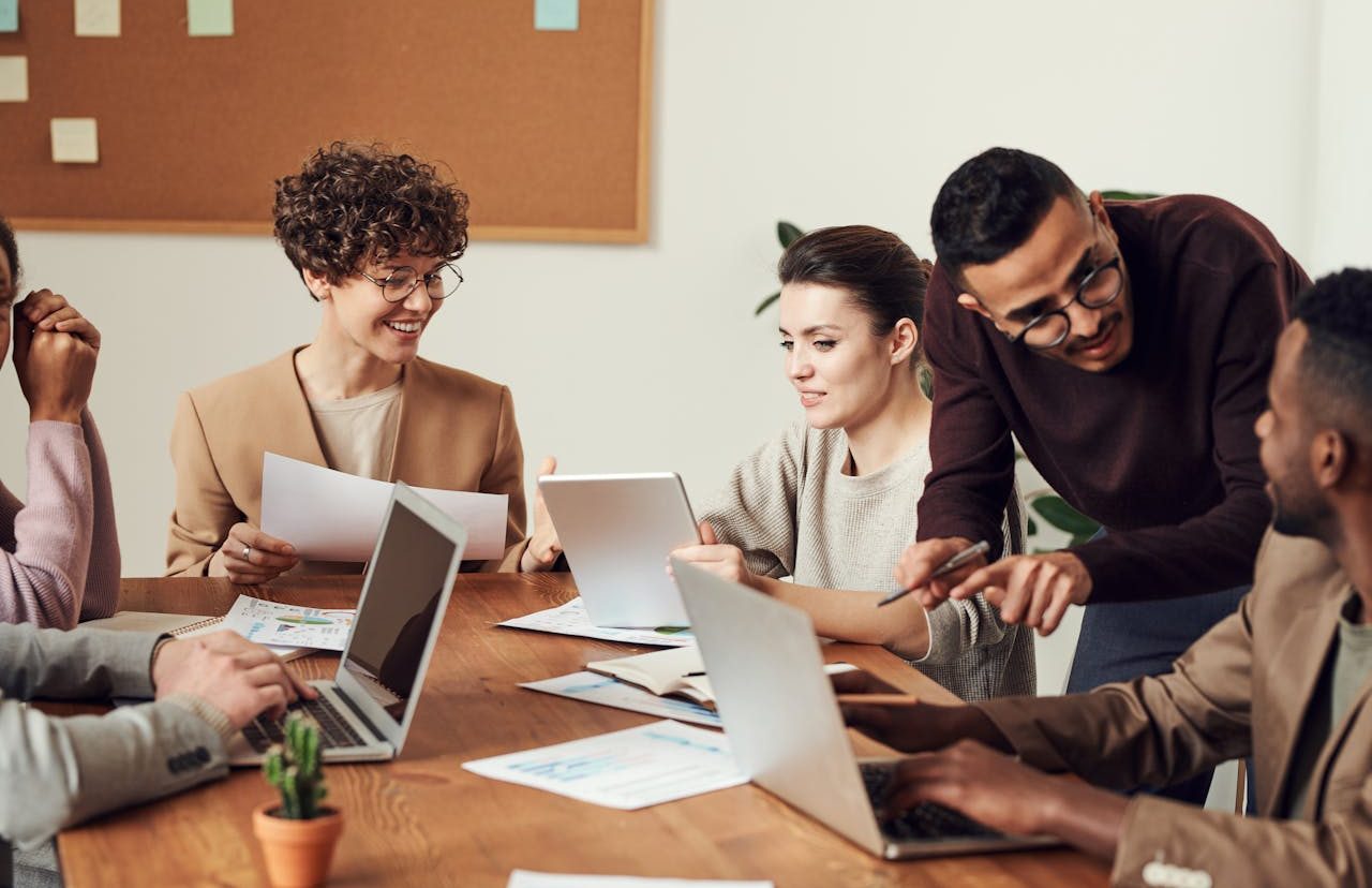 Grupo de personas sentadas alrededor de una mesa de oficina con sus ordenadores portátiles.