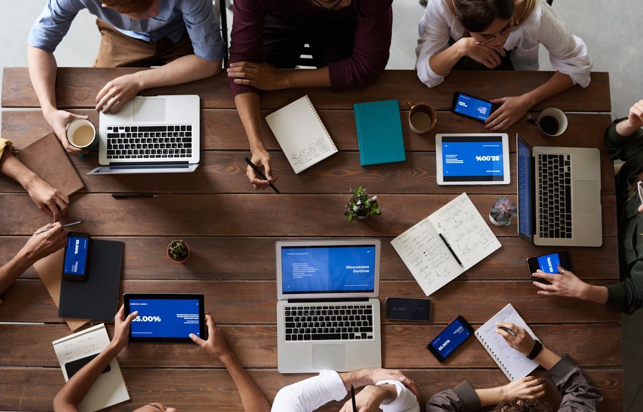 Mesa de trabajo con diversos empleados, cada uno con su ordendor portátil o su tablet PC.