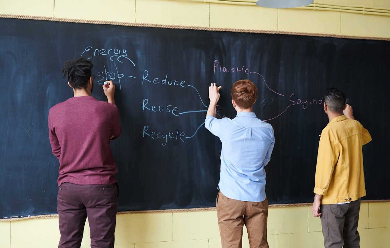 Tres estudiantes escribiendo con tiza en una pizarra