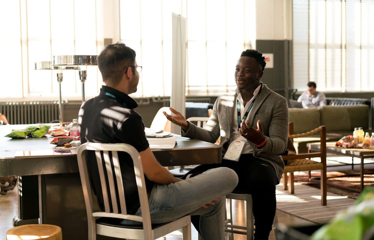 Dos hombres jóvenes conversando sentados en una oficina moderna