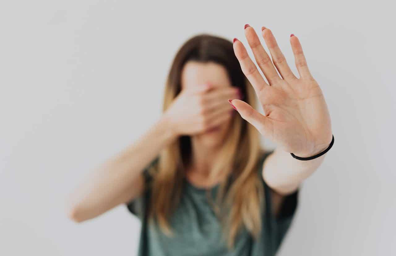 Mujer cubriéndose los ojos y extendiendo la mano hacia la cámara pidiendo que pare la violencia