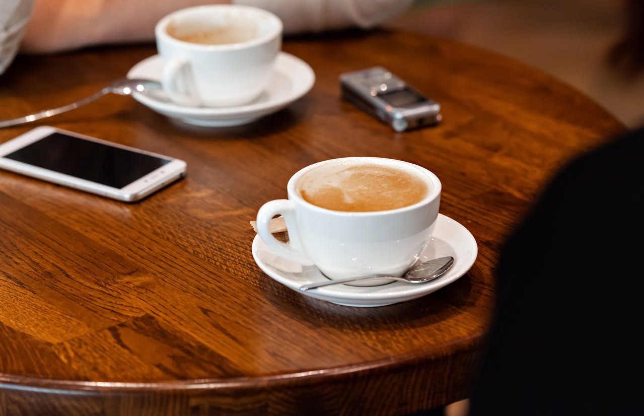 Personas alrededor de una mesa con dos tazas de café, una grabadora de voz y un teléfono móvil