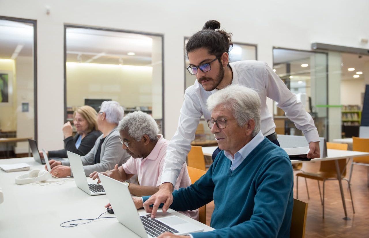 Tutor joven enseñando informática a personas mayores