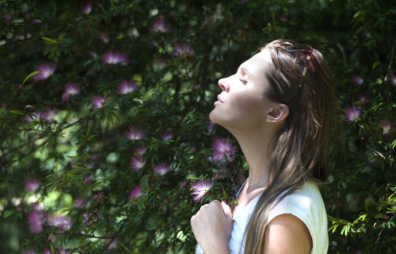 Mujer inspirando frente a un arbusto de flores