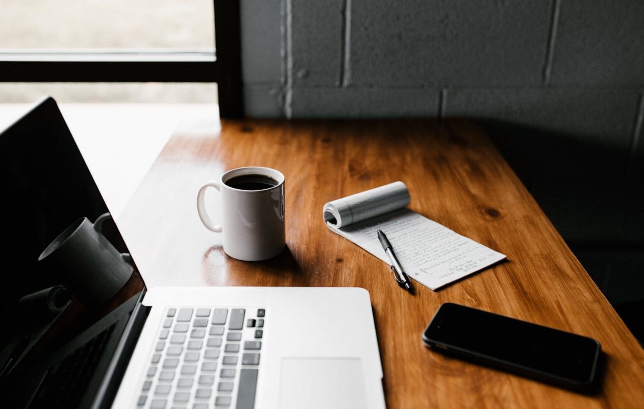 Mesa de trabajo con ordenador portátil, taza, anotador y teléfono móvil