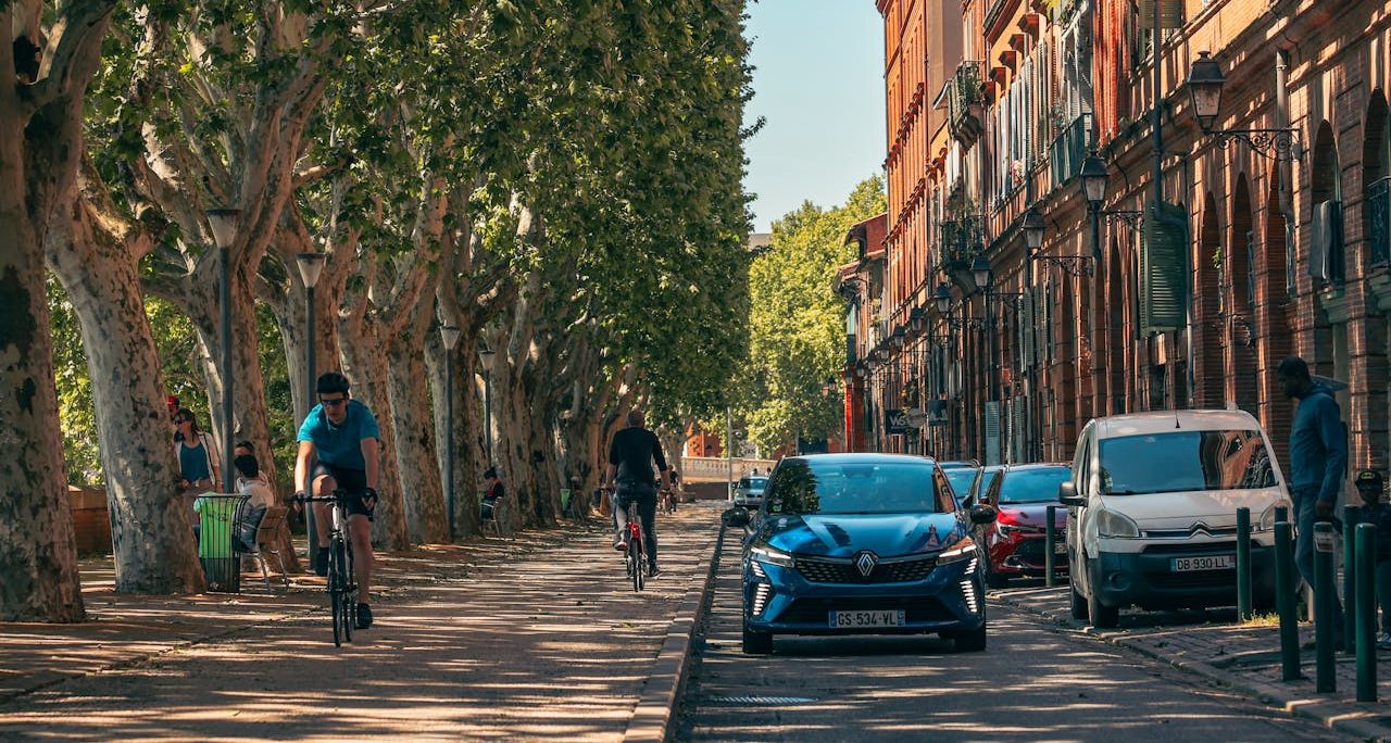 Parque frente a casas. Coches, bicicletas y transeúntes