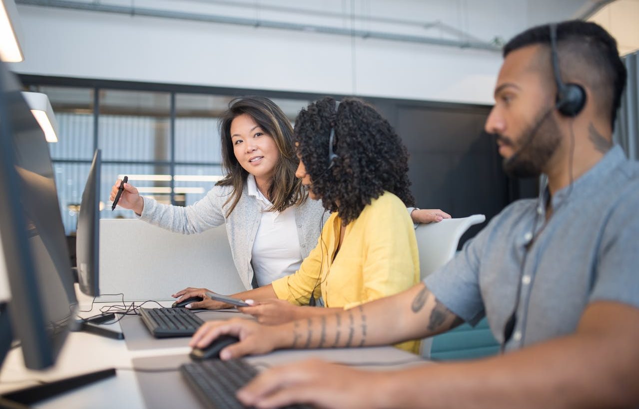 Mujer capacitando a dos empleados en una oficina con ordenadores