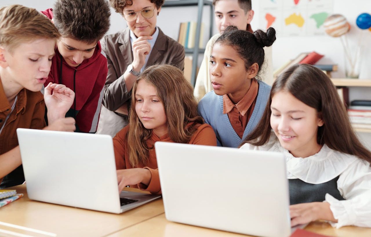 Varios estudiantes colaborando. Dos de ellas están usando ordenadores portátiles