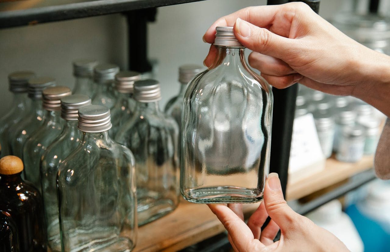 Persona tomando una botella vacía de un estante donde hay muchas otras