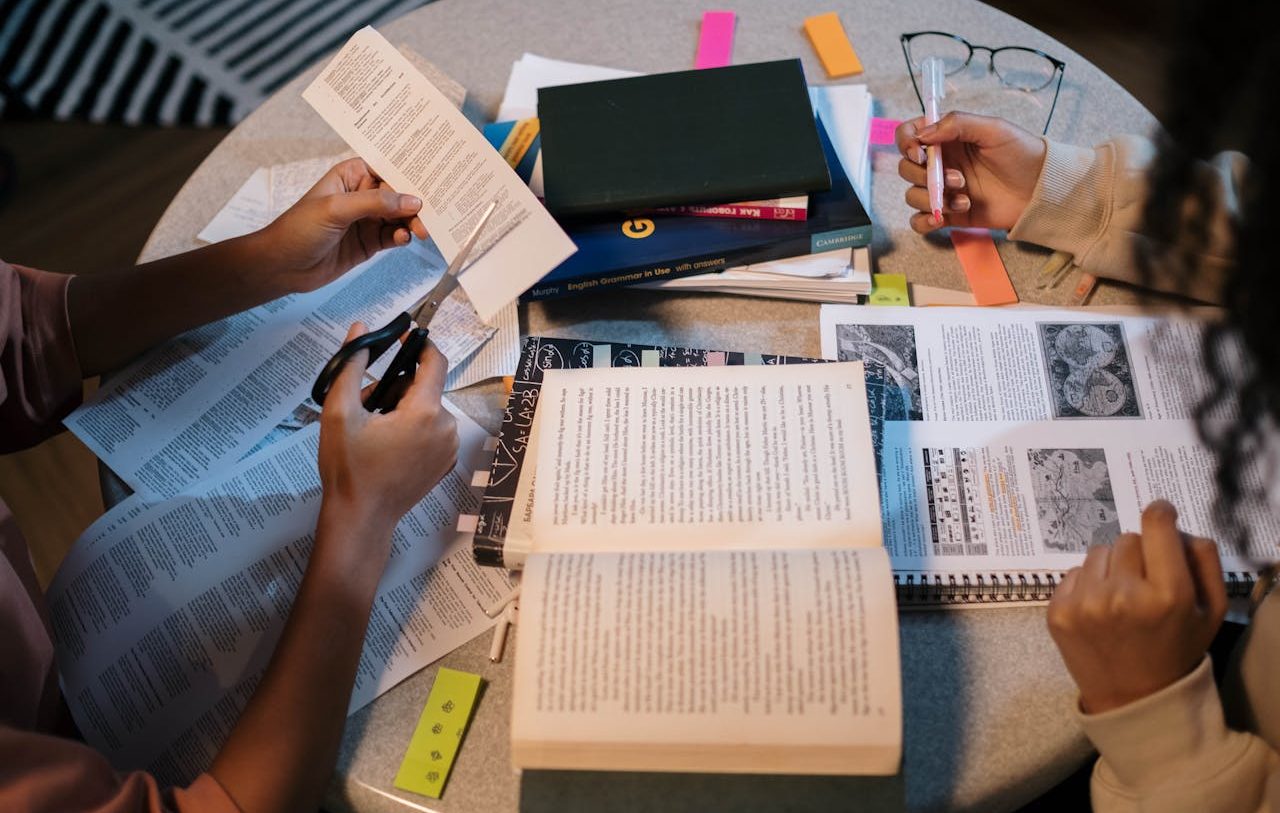 Personas con diversos materiales de consulta sobre una mesa, incluyendo un libro y un recorte