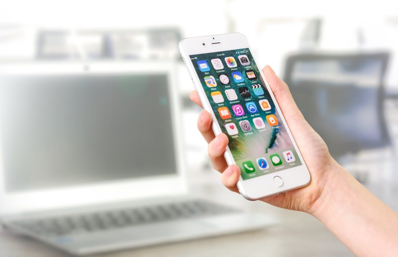 Persona sosteniendo un iPhone frente a un ordenador portátil blanco