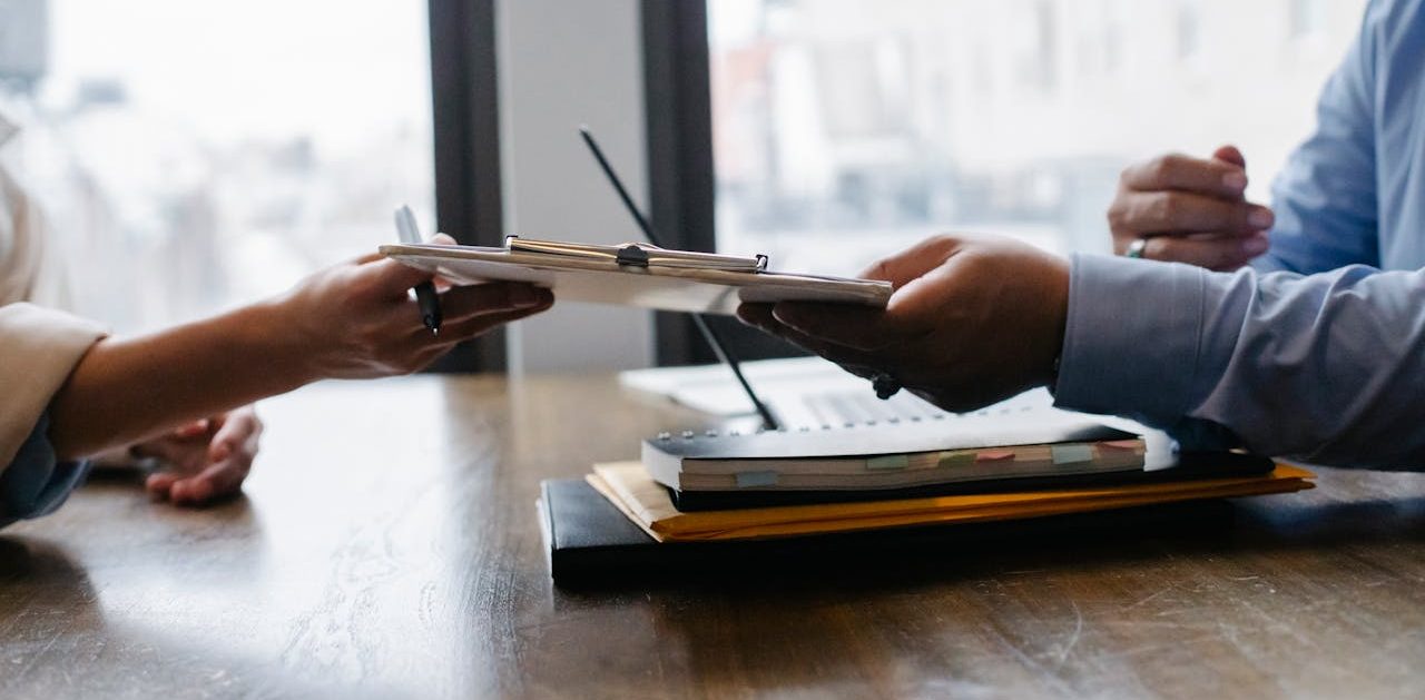 Persona entregando a otra una carpeta con documentos