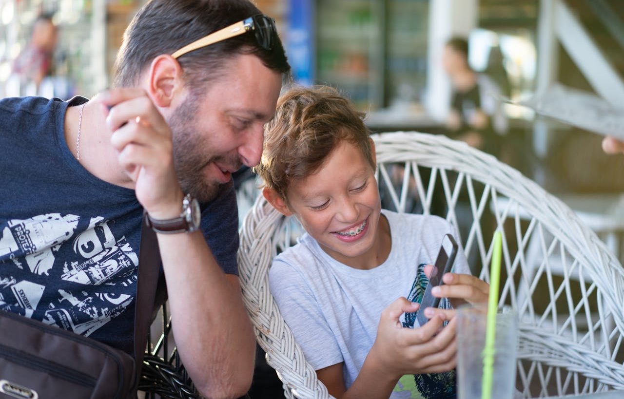 Hijo usando su teléfono móvil junto a su padre