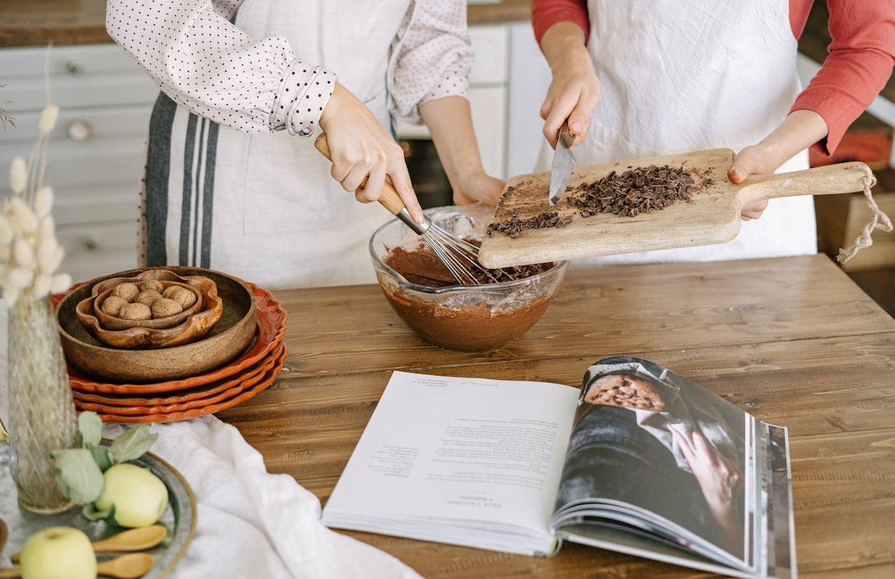 Dos personas preparando un plato frente al libro de recetas