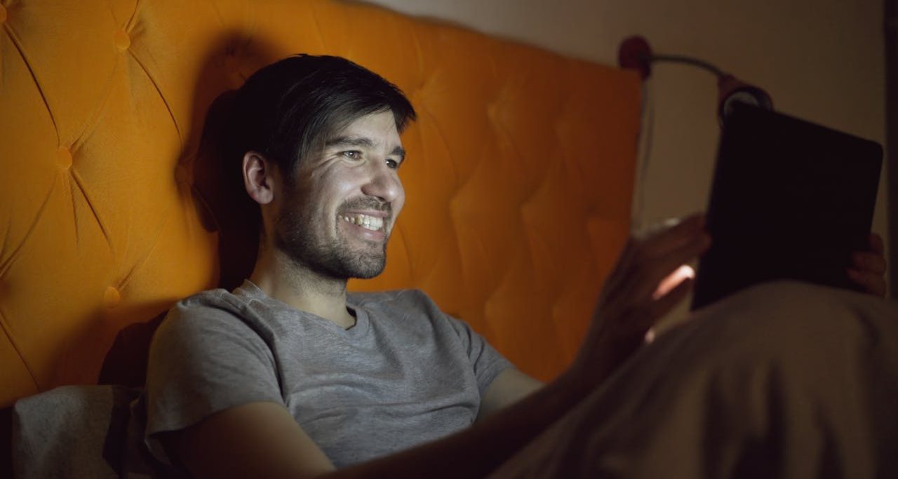 Hombre joven mirando vídeo en su cama a través de su tablet