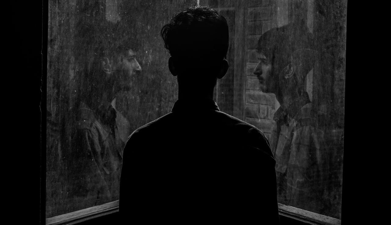 Hombre joven mirando su reflejo en dos ventanas